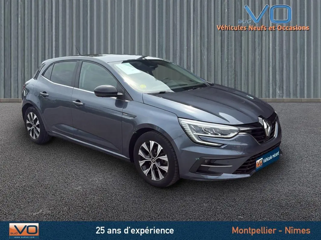 Renault Mégane IV Berline gris foncé vue 3/4 avant droit, jantes alliage 16 pouces et phares LED allumés.