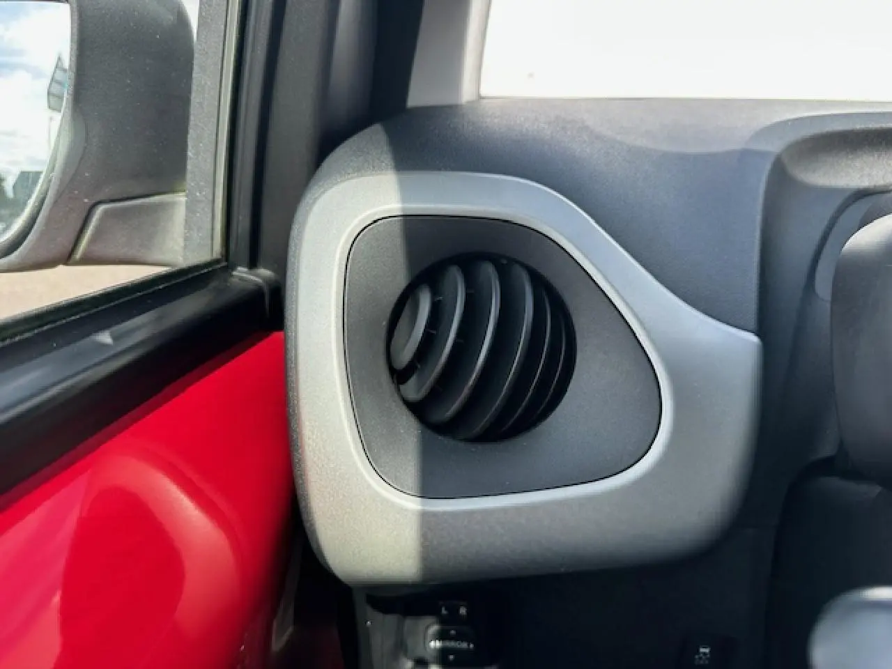 Détail de la sortie d'air ronde côté gauche sur tableau de bord gris d'une Citroën C1 rouge Scarlet 2014