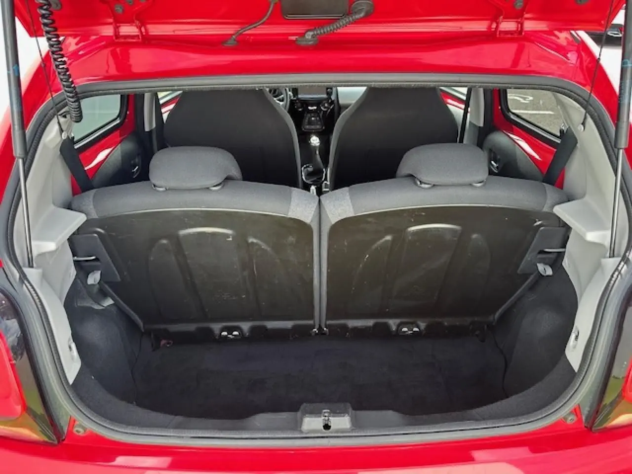 Coffre ouvert vu de l'arrière d'une Citroën C1 rouge Scarlet, montrant banquette arrière et intérieur noir.