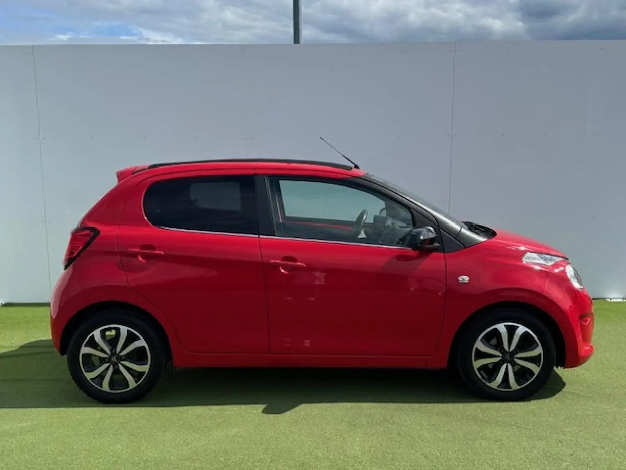 Profil côté gauche d'une Citroën C1 rouge Scarlet avec jantes alliage noires et toit ouvrant souple noir