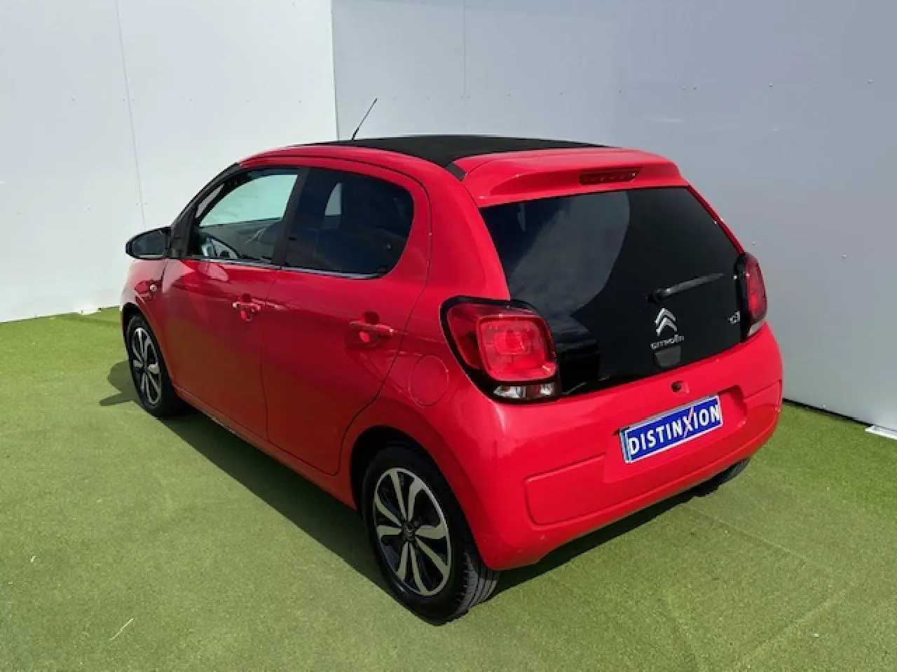 Vue 3/4 arrière droite d'une Citroën C1 rouge Scarlet avec toit noir et jantes alliage 15 pouces.