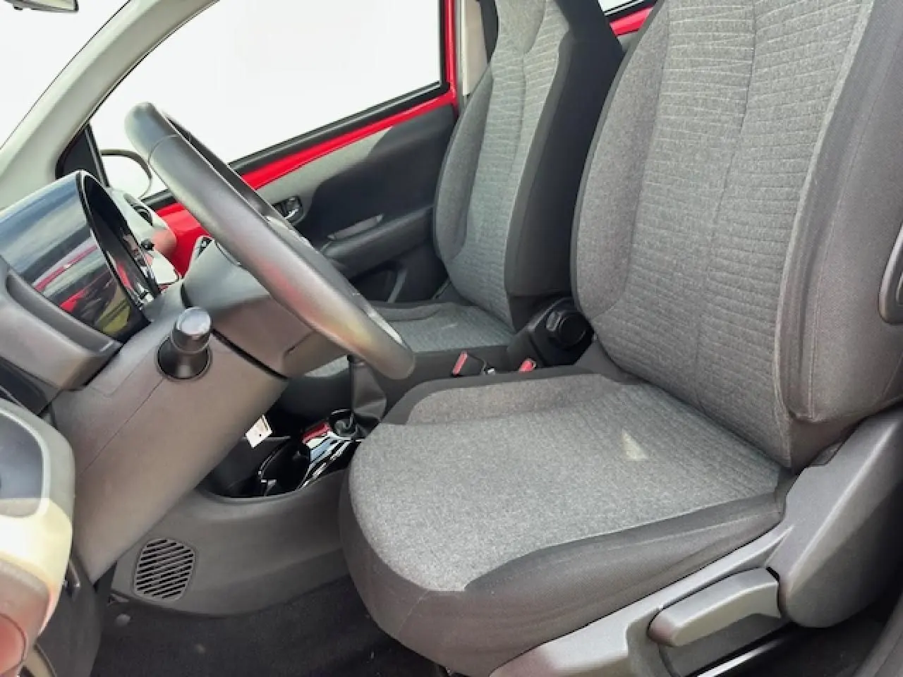 Intérieur côté conducteur de la Citroën C1 rouge Scarlet, sièges tissu gris et volant en croûte de cuir visible de profil.