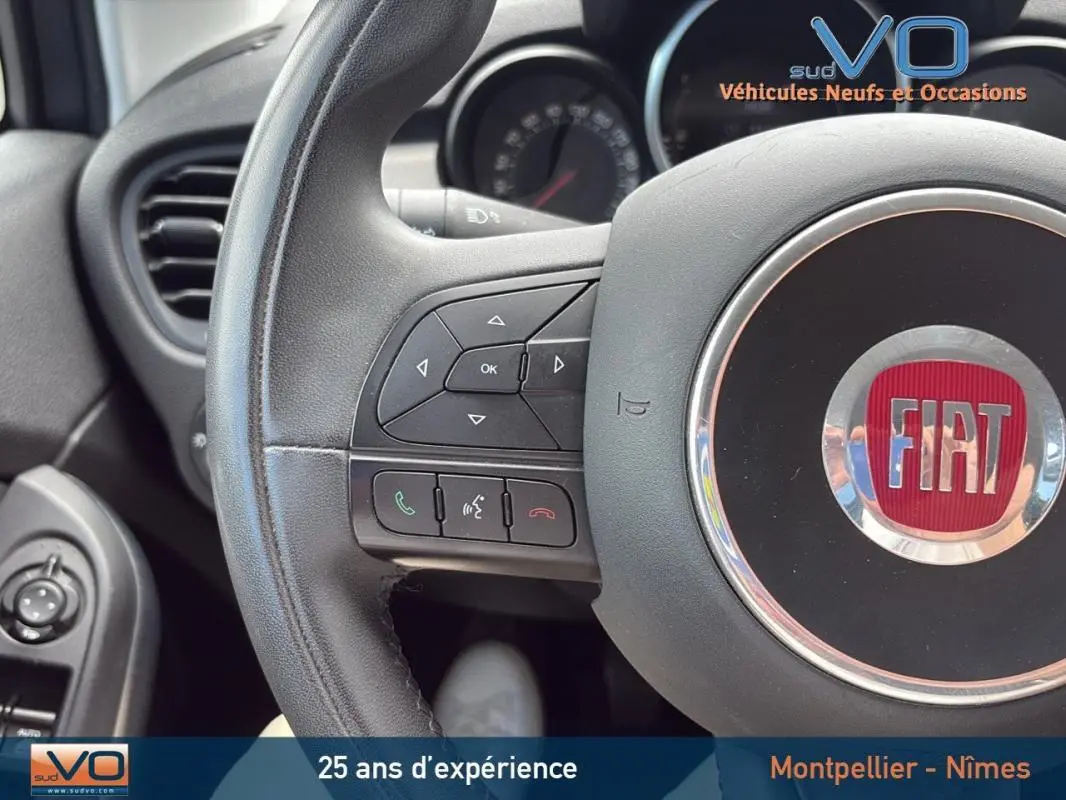 Gros plan sur le volant cuir de la Fiat 500X 2015, montrant les commandes intégrées et le logo central rouge.