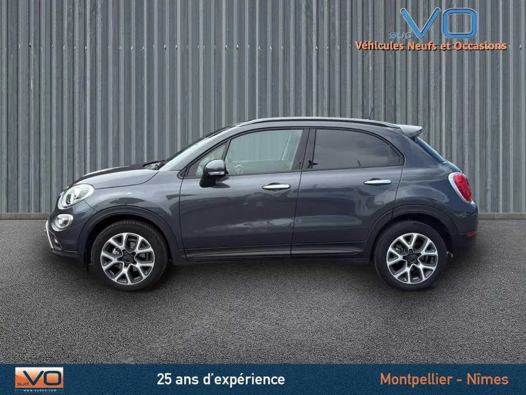 Profil côté gauche d'un FIAT 500X Cross gris anthracite avec jantes alliage 17 pouces sur fond industriel.