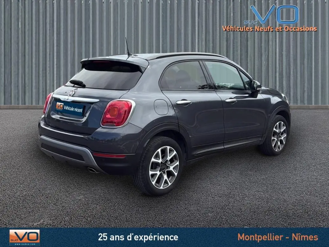Vue 3/4 arrière droite d'une FIAT 500X Cross gris anthracite avec jantes alliage 17 pouces sur sol bitumé.