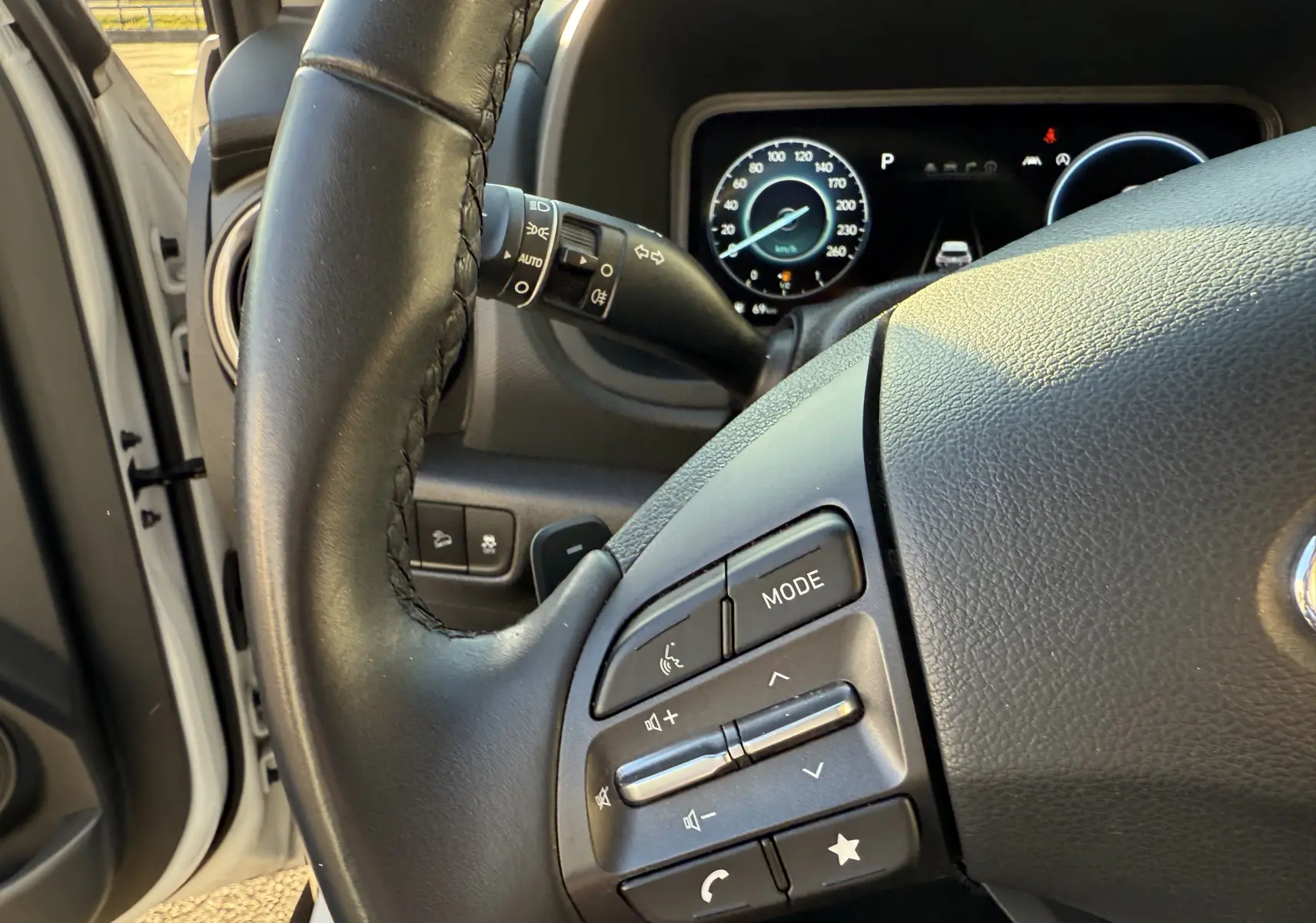 Gros plan sur le volant noir et le tableau de bord numérique du Hyundai Kona blanc Atlas, côté gauche, intérieur éclairé.