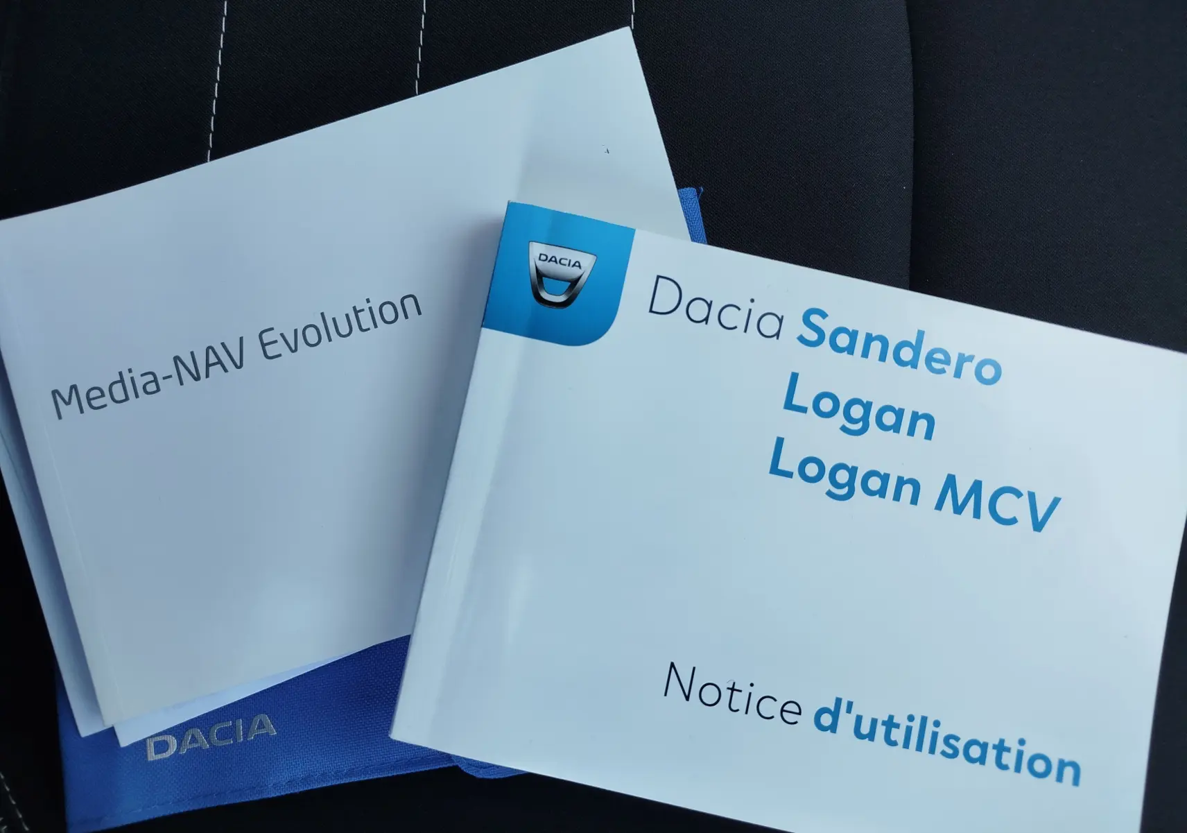 Manuels d'utilisation Dacia Sandero, Logan et Media-NAV posés sur un siège en tissu noir.