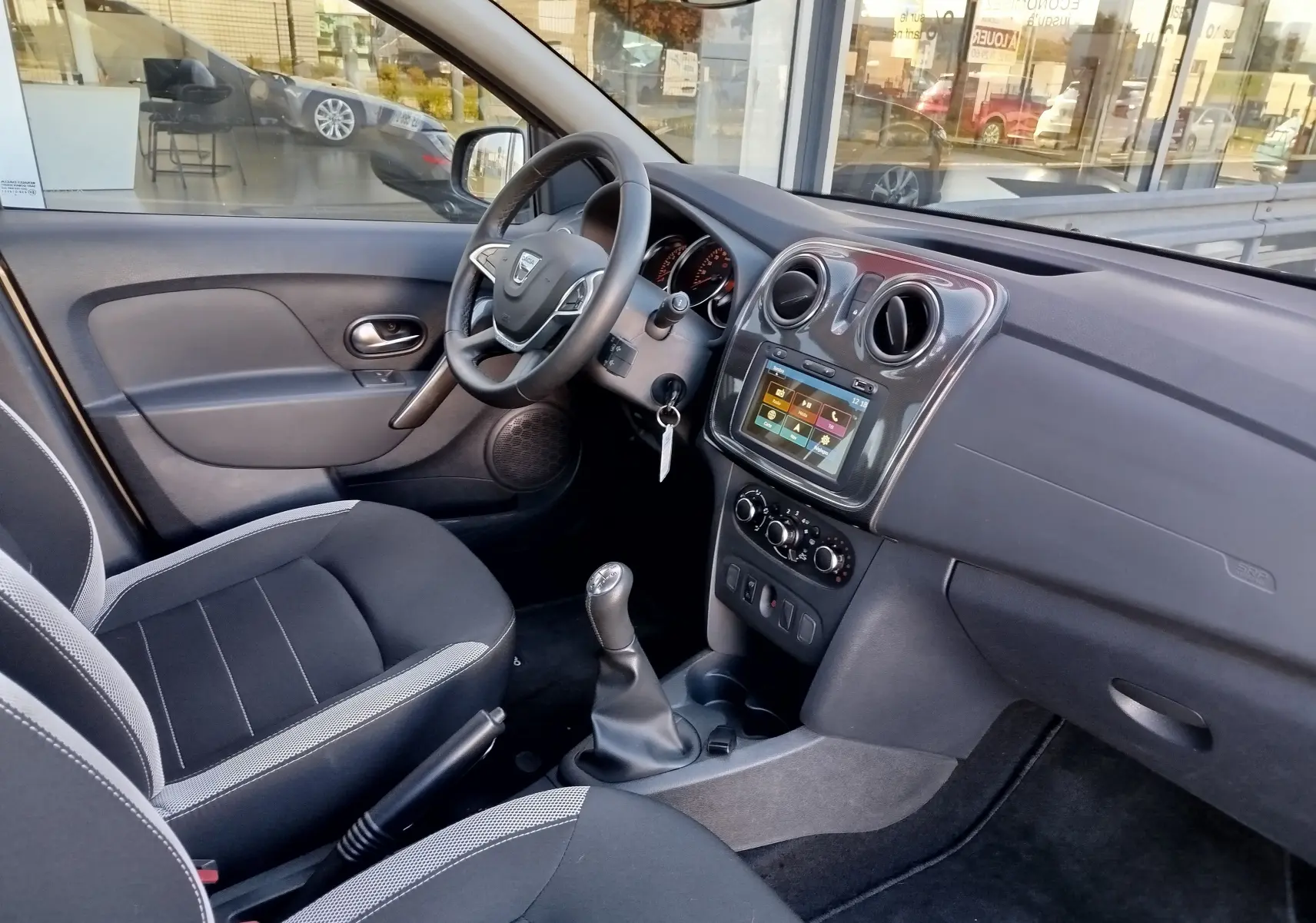 Intérieur côté conducteur de la Dacia Sandero Stepway 2020, tableau de bord gris avec écran tactile et sièges tissu gris.
