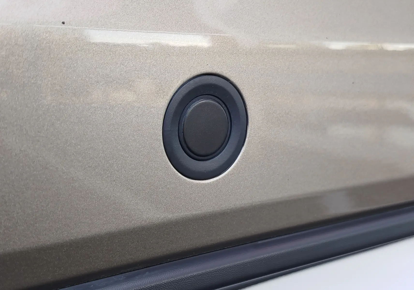 Gros plan sur un capteur de stationnement noir intégré dans la carrosserie beige dune d'une Dacia Sandero Stepway 2020.