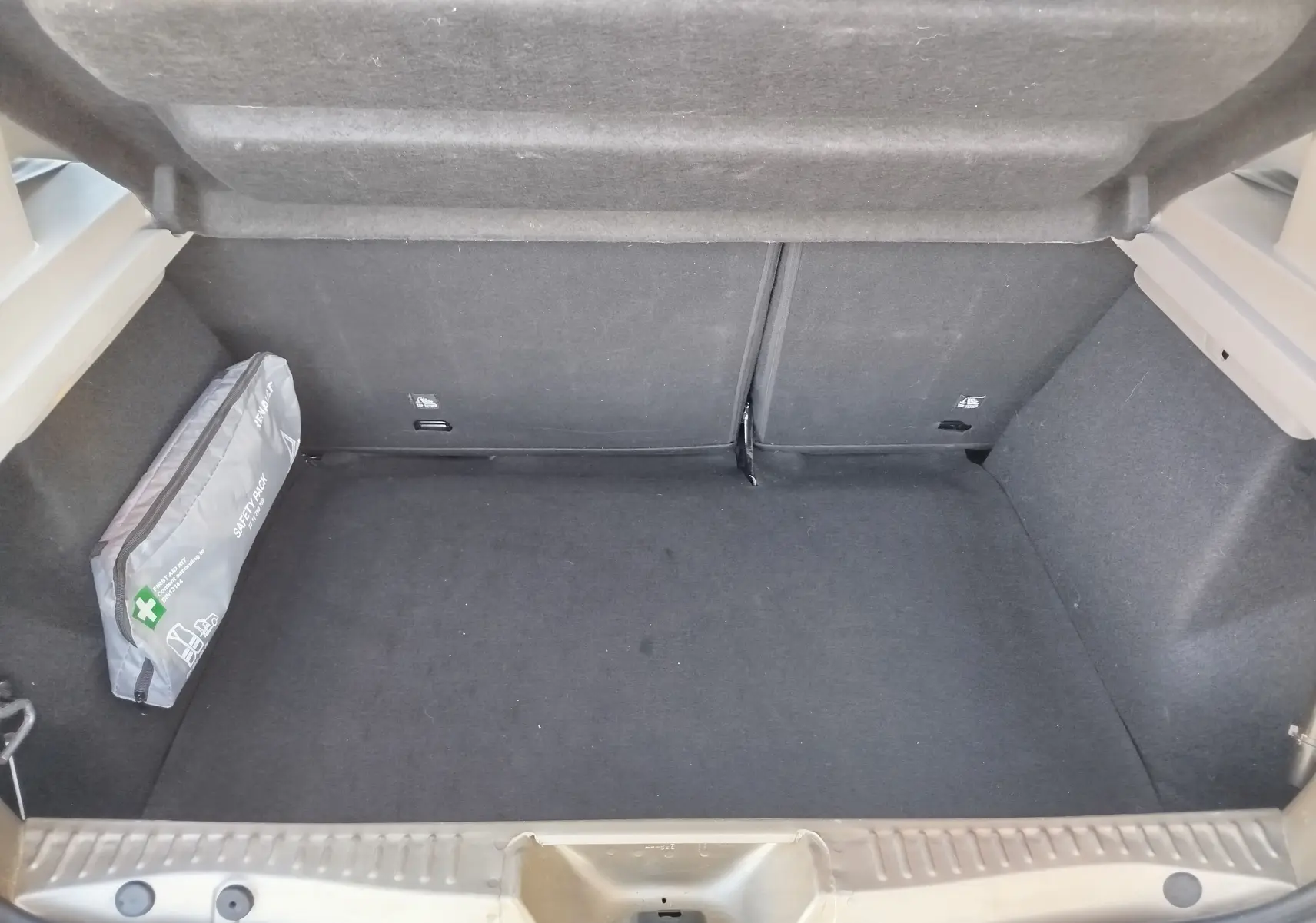 Coffre ouvert d'une Dacia Sandero Stepway beige dune 2020, montrant un espace de chargement propre avec une trousse de sécurité grise sur le côté gauche.