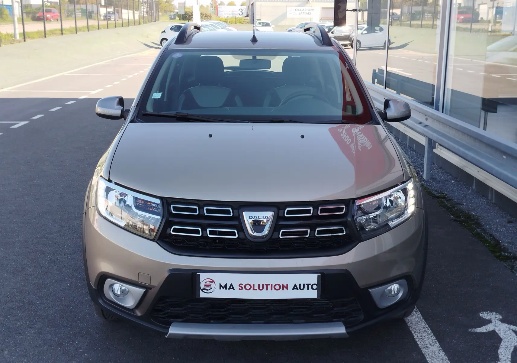 Vue frontale d'une Dacia Sandero Stepway beige dune 2020 avec calandre noire et feux LED allumés.