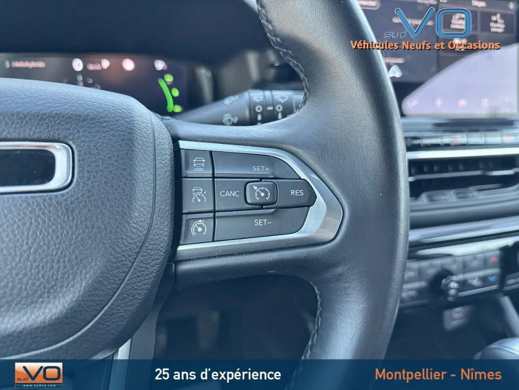 Gros plan sur les commandes du régulateur de vitesse au volant cuir du Jeep Compass blanc, tableau de bord en arrière-plan.