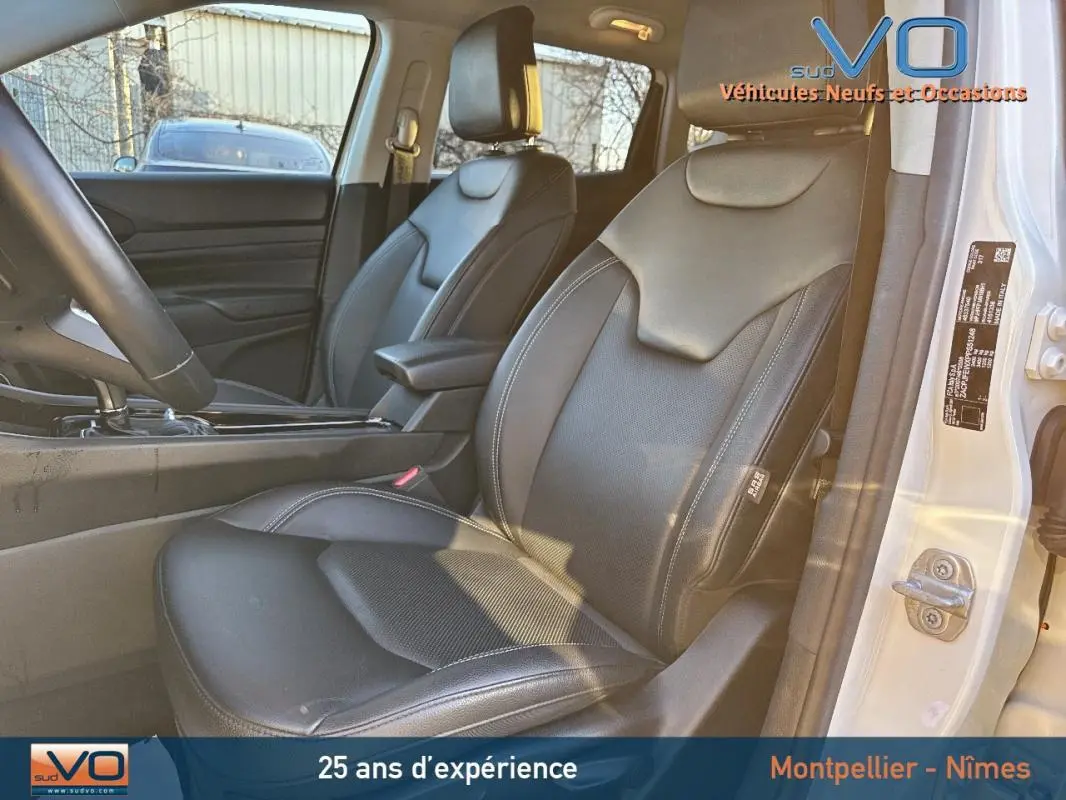 Vue intérieure côté conducteur du Jeep Compass blanc 2023, sièges cuir noirs avec accoudoir central visible.