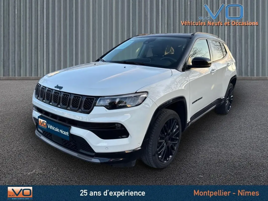 Jeep Compass blanc en 3/4 avant droit avec jantes alliage noires et barres de toit visibles.
