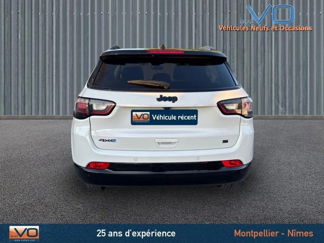 Vue arrière d'un Jeep Compass blanc 2023 avec logo 4xe et finition S, sur fond industriel gris.
