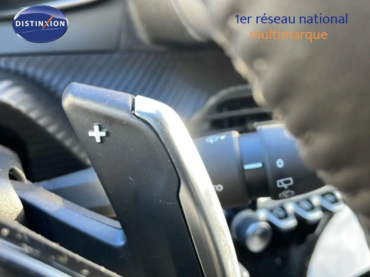 Gros plan sur la palette de changement de vitesse + au volant d’une Peugeot 208 noire, intérieur gris noir.