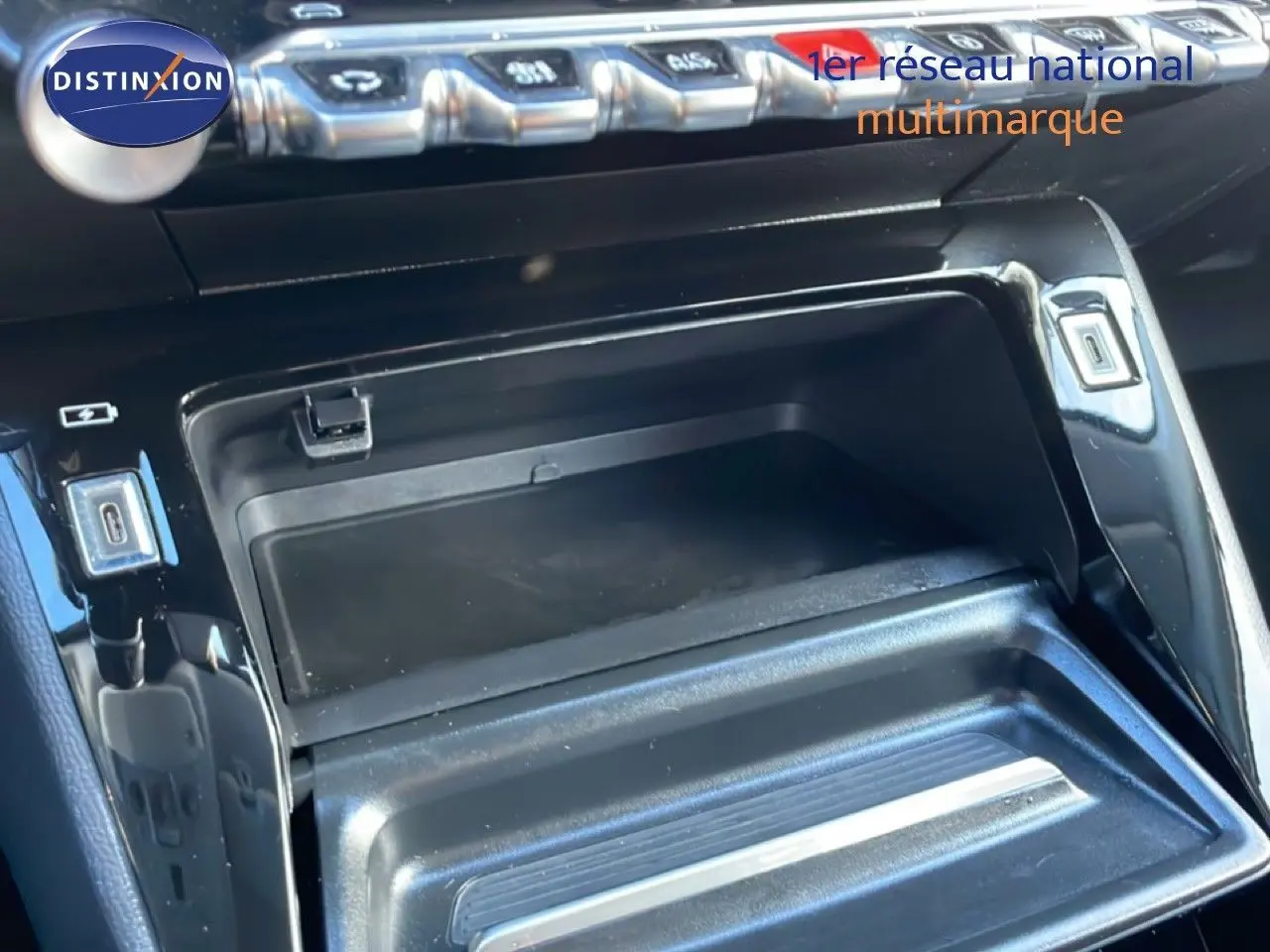 Vue rapprochée de la console centrale noire de la Peugeot 208 1.2 Hybrid 110ch, avec compartiment ouvert et boutons argentés.