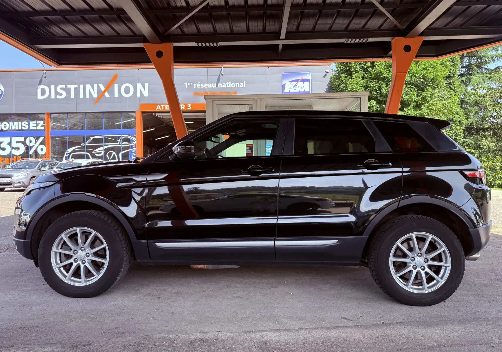 Range Rover Evoque noir vu de profil côté gauche, stationné sous un abri avec structure orange.