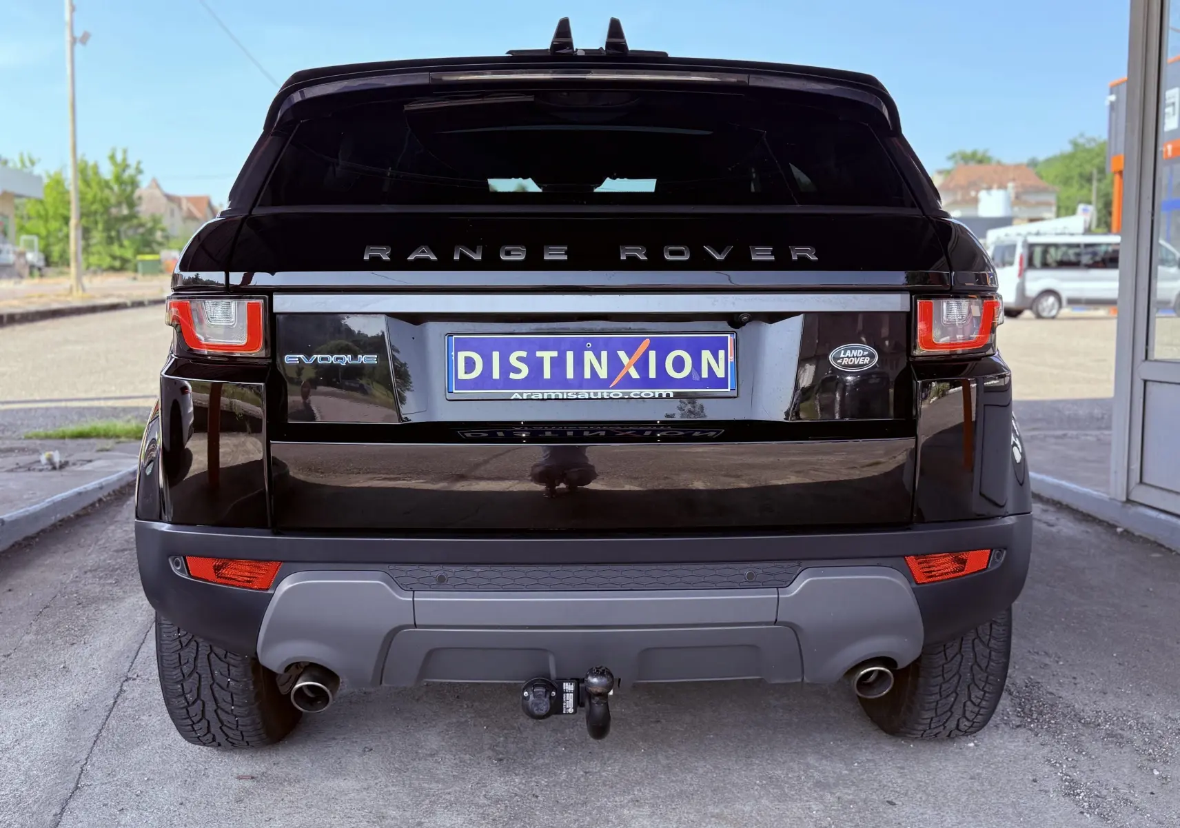 Vue arrière d'un Range Rover Evoque noir avec attelage et feux arrière allumés sur un parking extérieur.