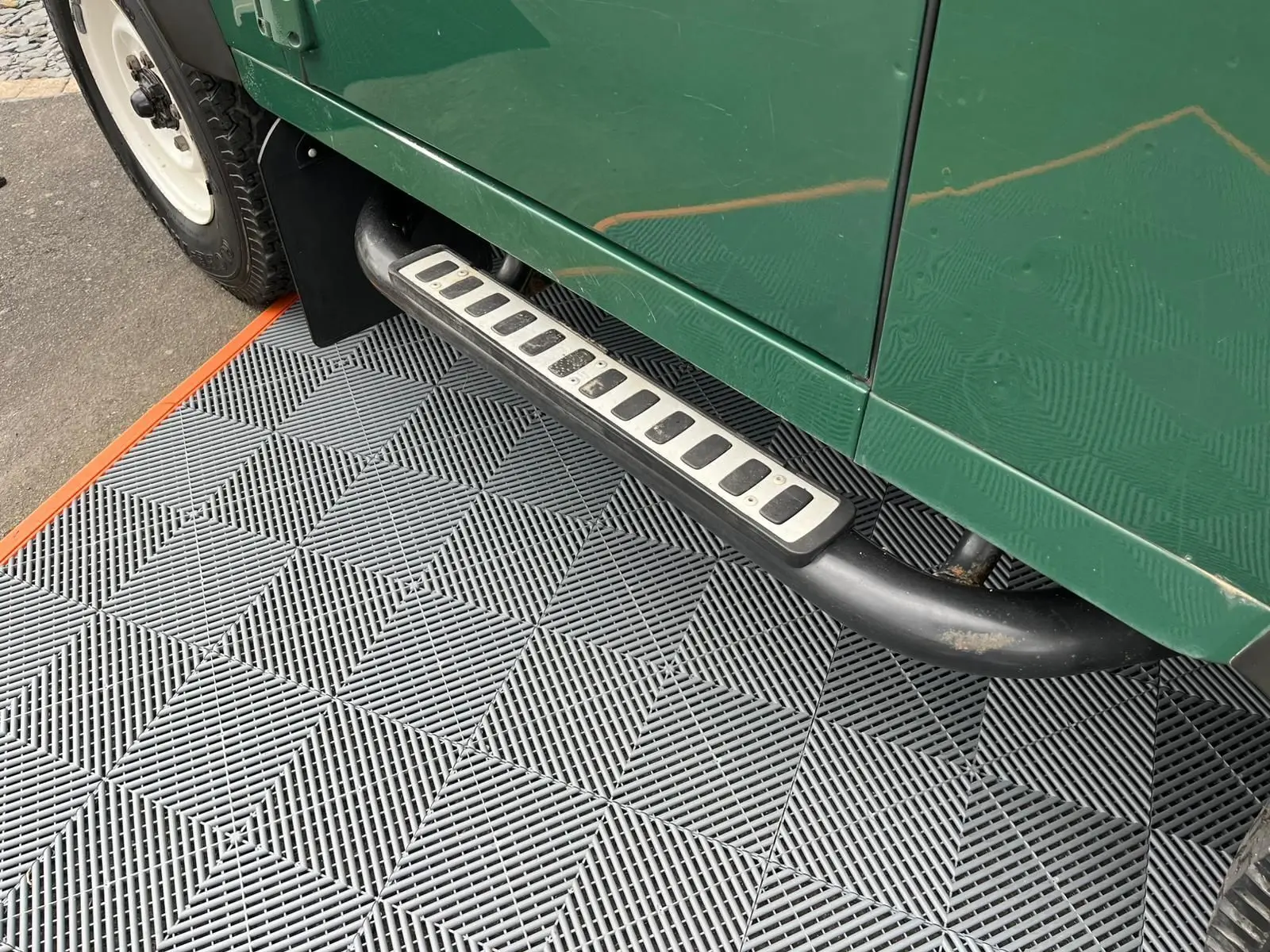 Vue rapprochée du marchepied côté gauche d’un Land Rover Defender 90 vert 2004 Hard Top avec pneus tout-terrain.