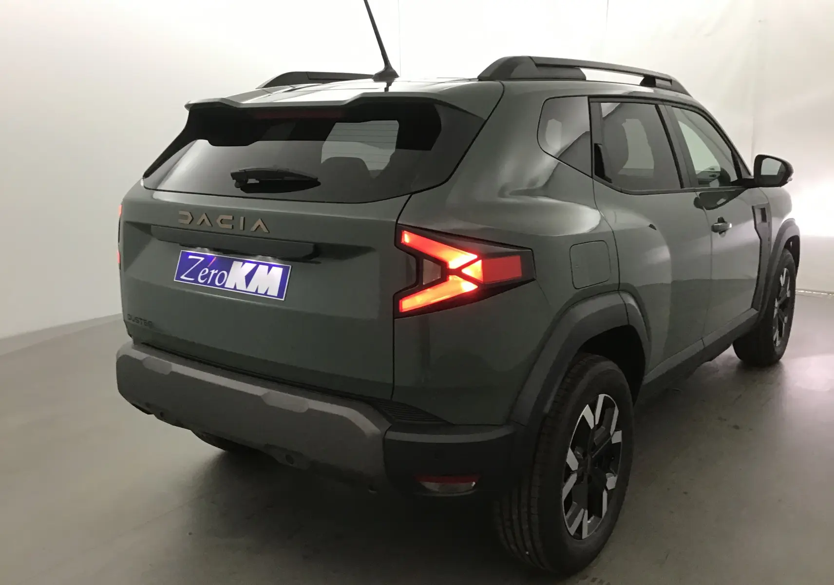 Vue 3/4 arrière droite du Dacia Duster 2025 kaki lichen avec feux arrière allumés et jantes noires distinctives.