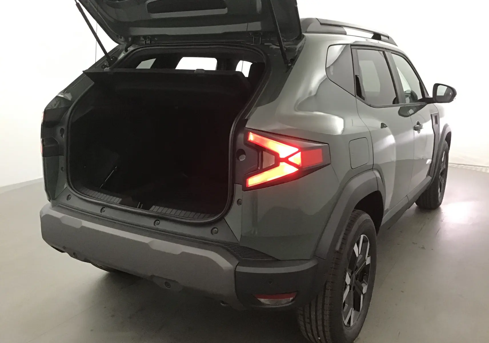 Vue arrière droite d'un Dacia Duster kaki lichen 2025 avec coffre ouvert et feux arrière allumés.