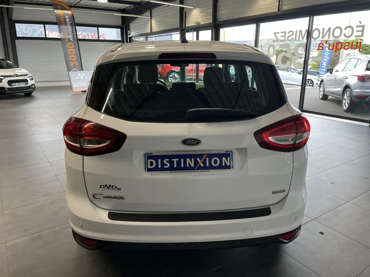 Vue arrière d'un Ford C-MAX blanc 2018 en showroom avec feux arrière rouges et vitre arrière teintée.