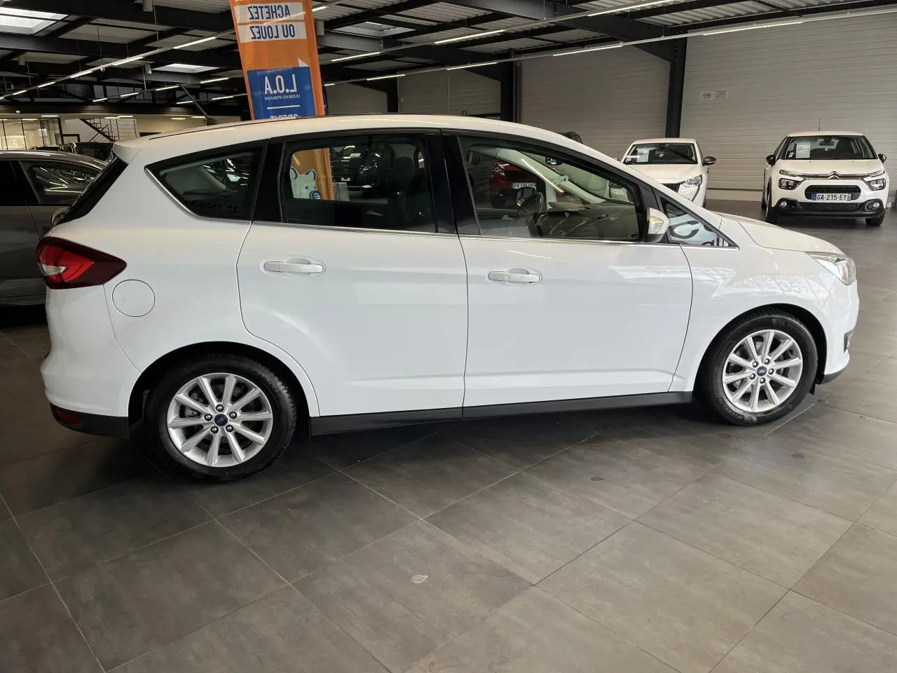 Ford C-MAX blanc vu de profil côté gauche dans un showroom avec jantes alliage 16 pouces.