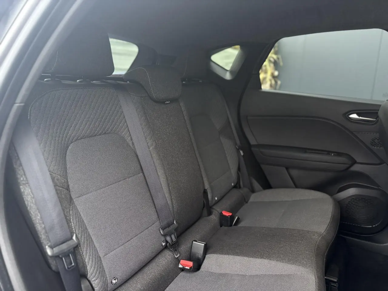 Vue intérieure côté droit des sièges arrière en tissu gris foncé du Renault Captur 2025, avec ceinture et porte de voiture visible.