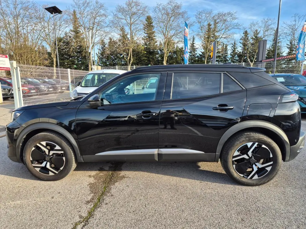 Vue de profil côté gauche d’un Peugeot 2008 Hybrid 145 e-DCS6 GT noir avec jantes alliage 18 pouces et barres de toit.