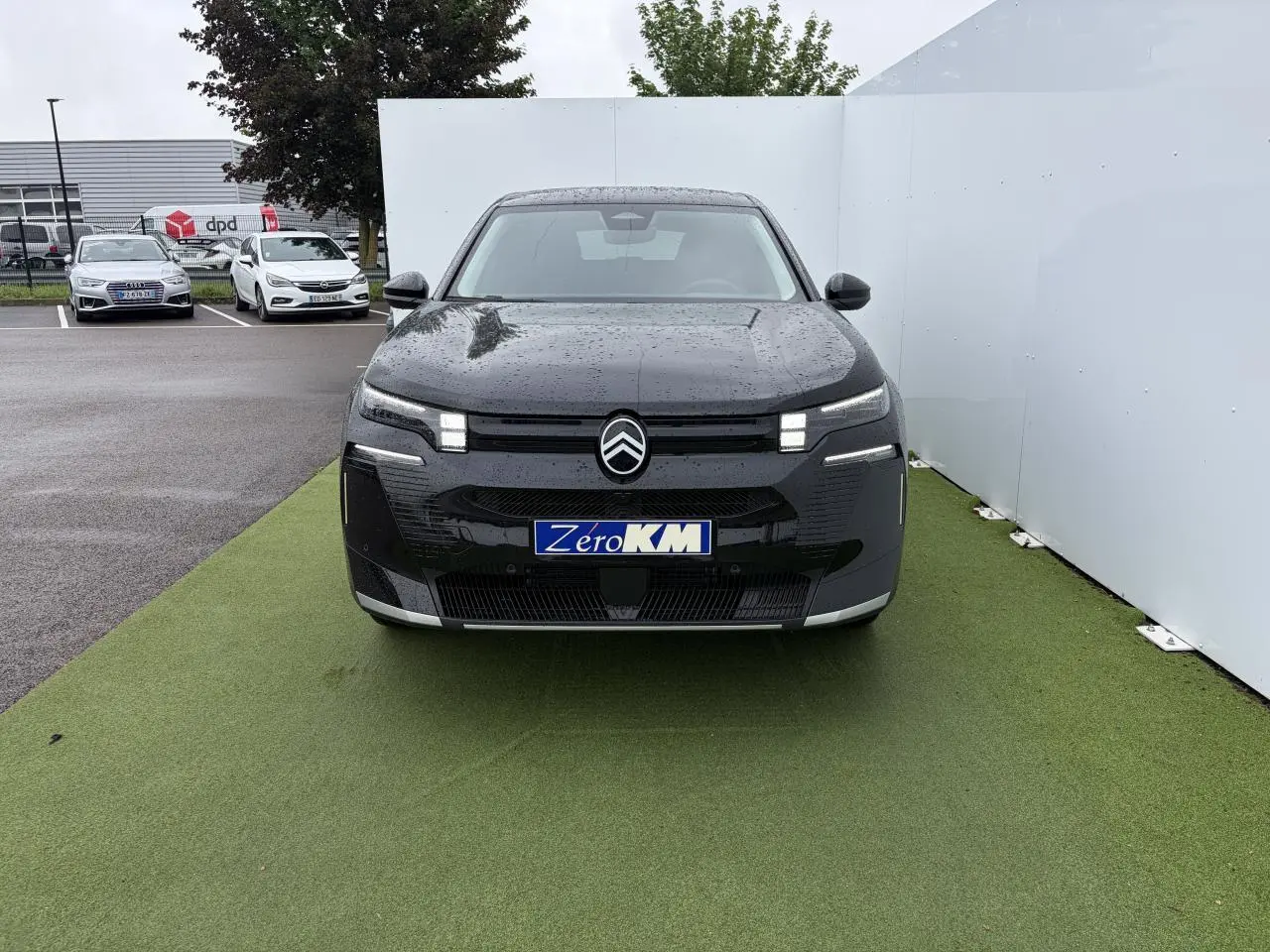 Vue avant d'un Citroën C5 Aircross noir métal avec feux LED distinctifs et logo centré sous la pluie.