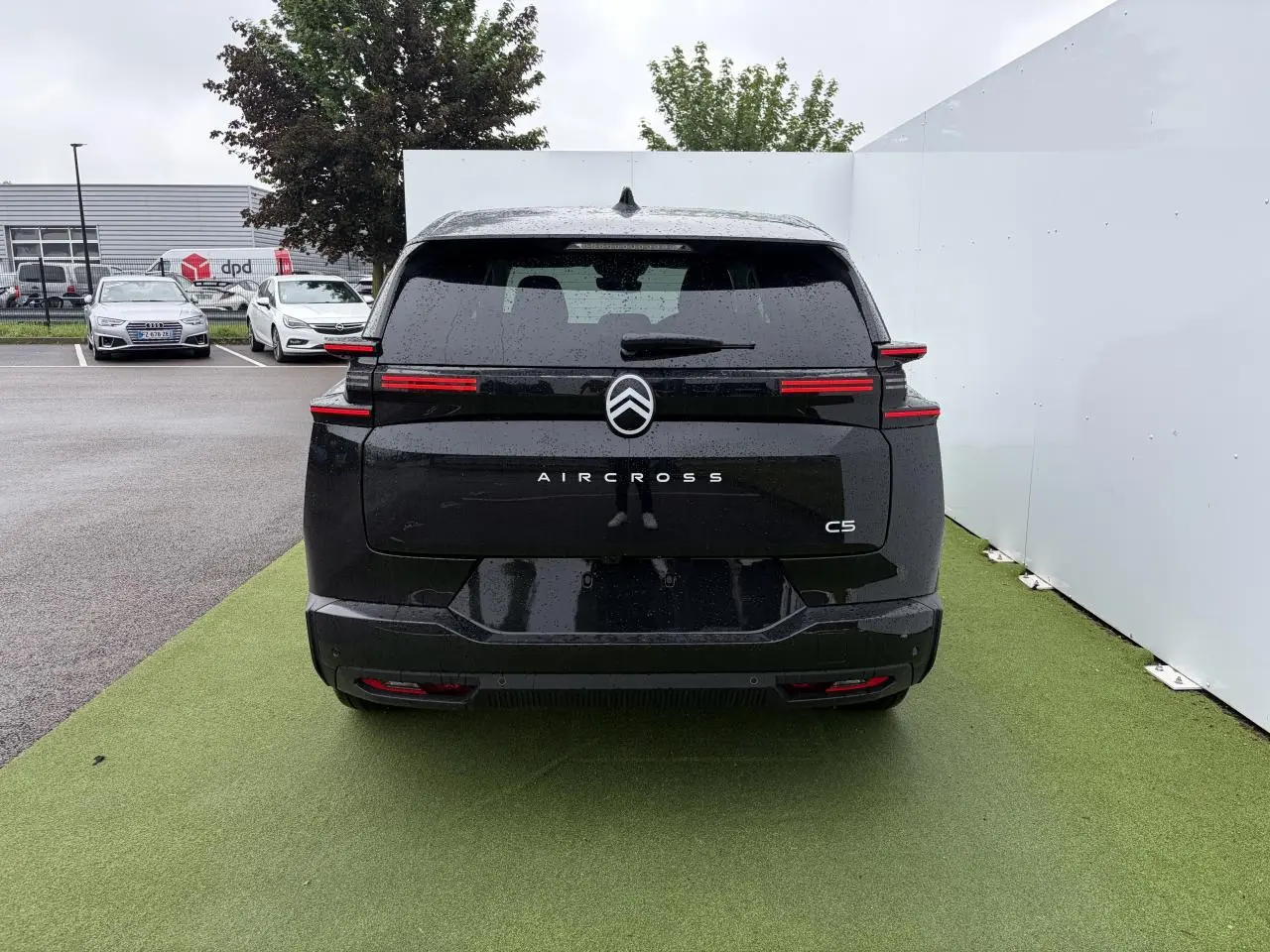 Vue arrière d'un Citroën C5 Aircross noir métal avec feux arrière LED horizontaux et toit panoramique visible sous la pluie.