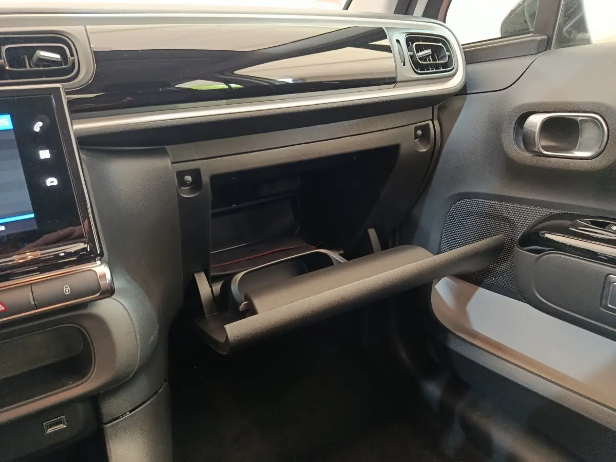 Intérieur de la Citroën C3 blanc, vue côté passager sur la boîte à gants ouverte et tableau de bord noir brillant.