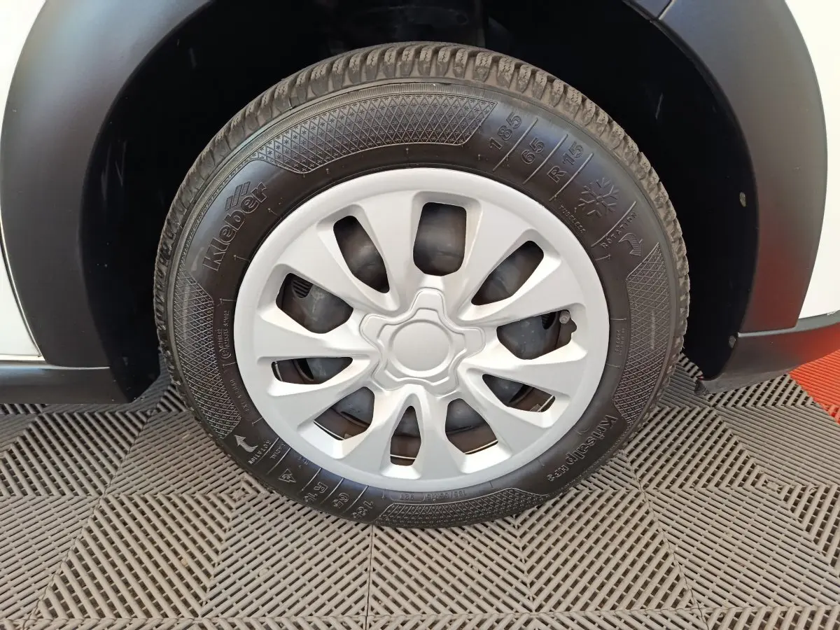 Gros plan sur la roue avant droite d'une Citroën C3 blanche, avec jante en plastique et pneu Kleber visible.