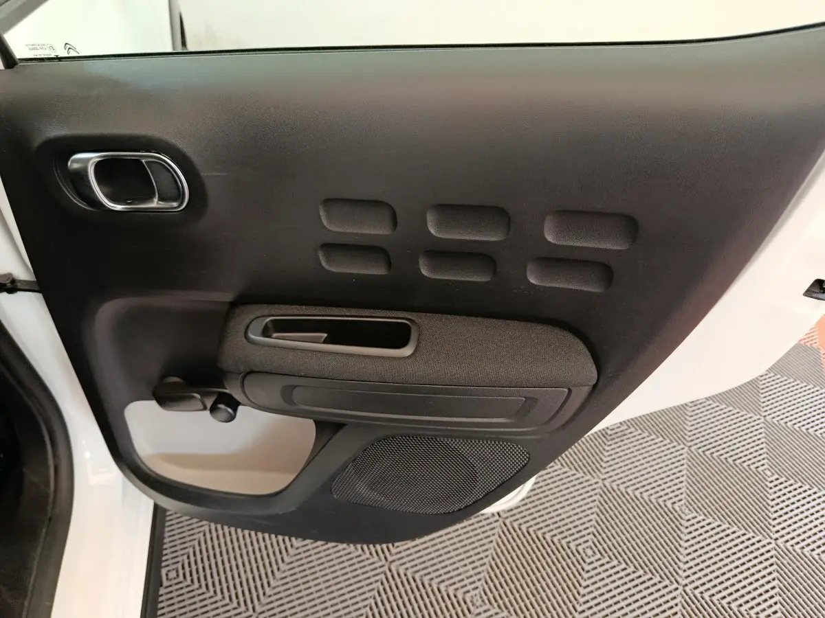 Vue intérieure de la porte avant gauche noire de la Citroën C3 blanche, mettant en valeur la poignée et le haut-parleur intégré.
