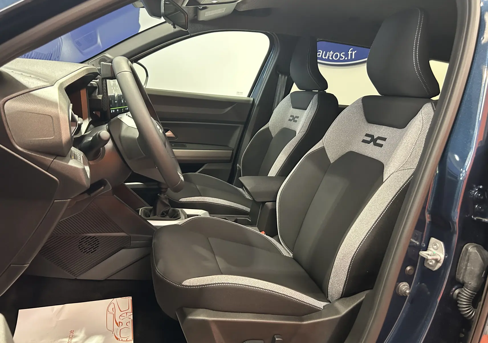 Vue intérieure côté conducteur du Dacia Bigster bleu indigo, mettant en valeur les sièges bi-ton tissu avec logo brodé.