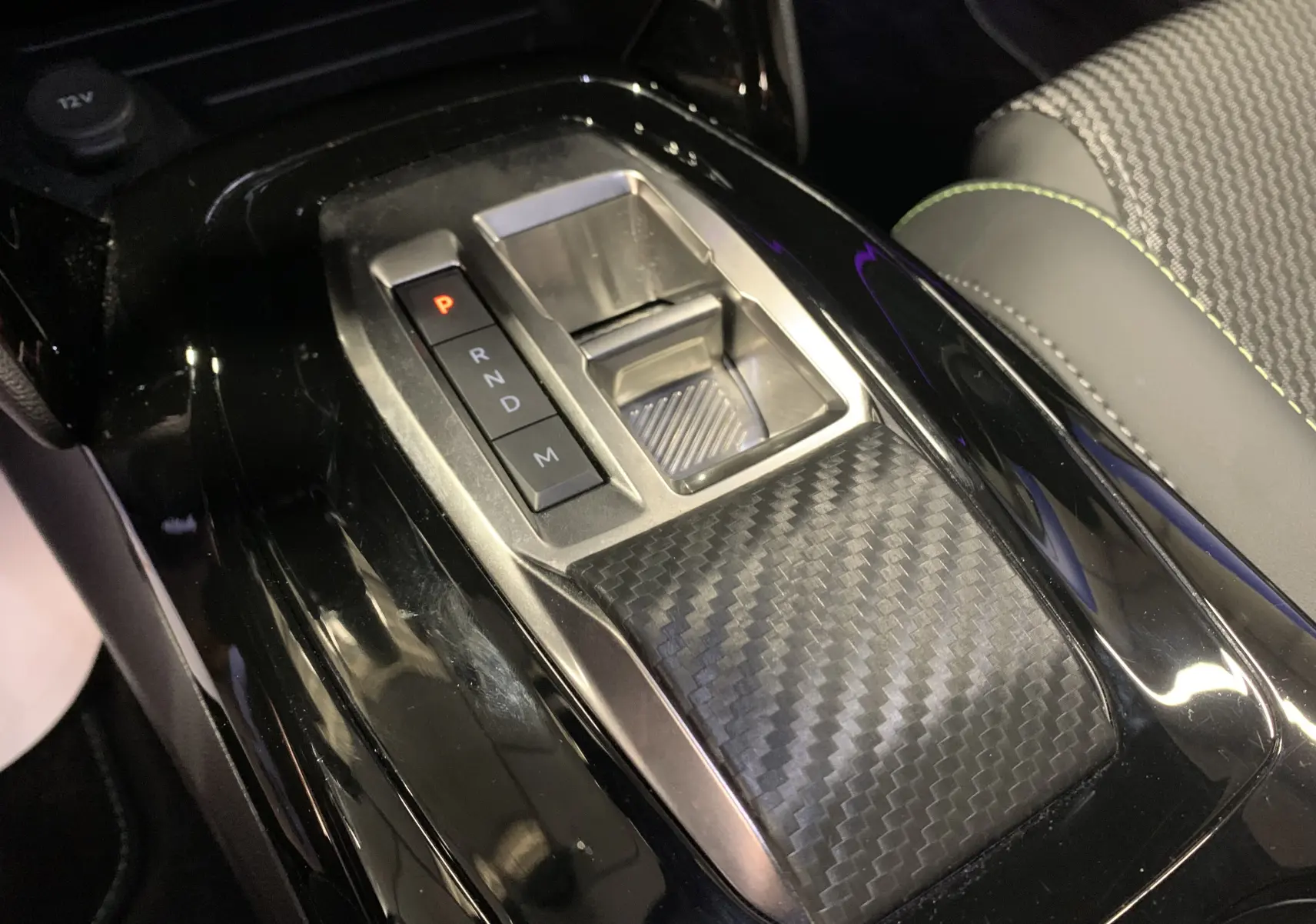 Gros plan sur la console centrale noire brillante avec levier de vitesses électronique et insert effet carbone dans un Peugeot 2008 2023.