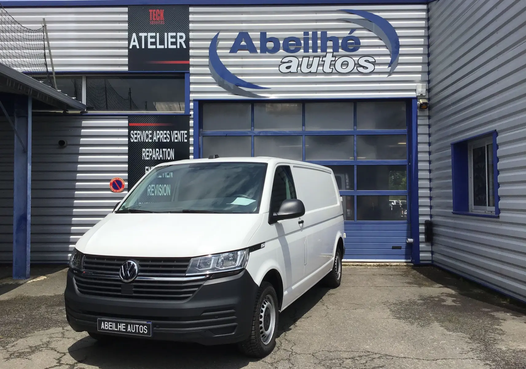 Volkswagen Transporter 6.1 blanc en 3/4 avant droit devant un atelier de réparation automobile.