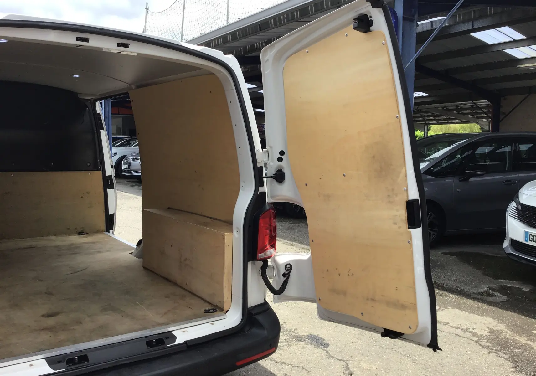 Vue arrière droite ouverte du Volkswagen Transporter 6.1 blanc, montrant l'intérieur utilitaire avec habillage bois.