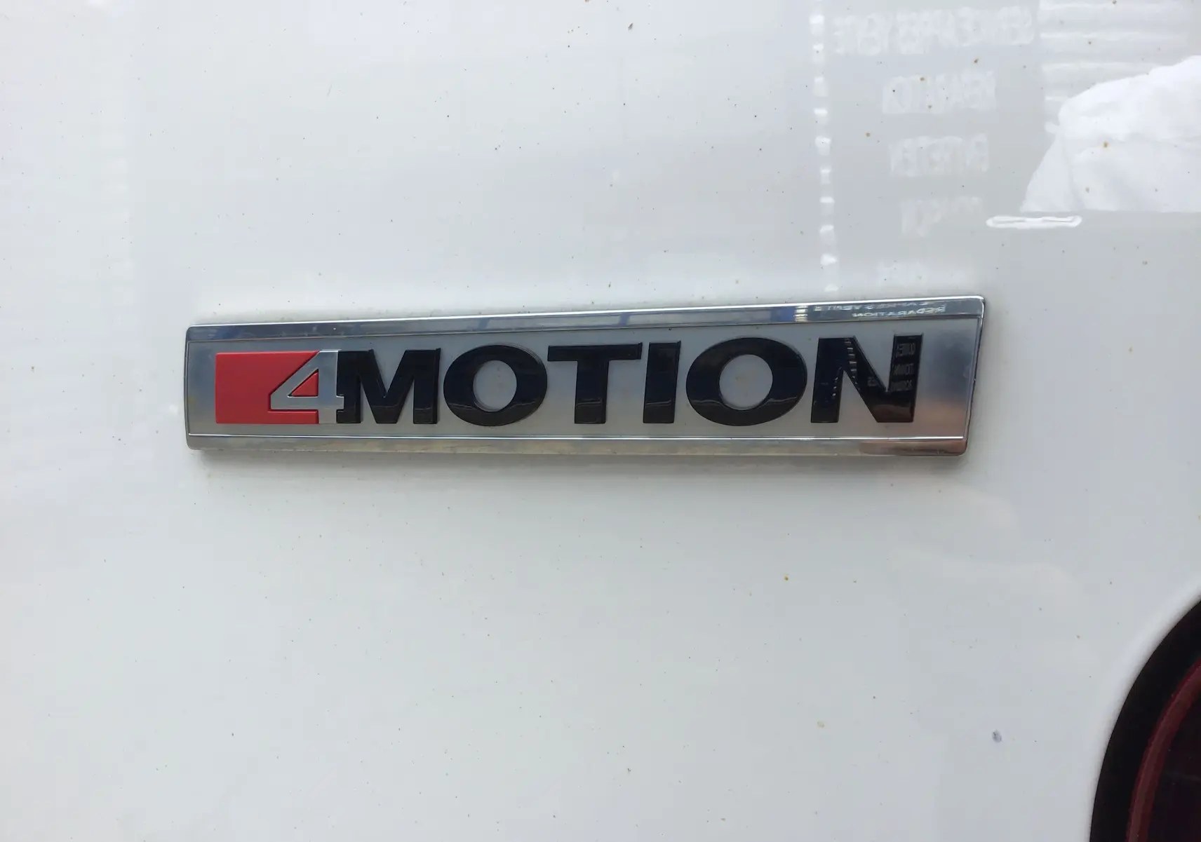 Gros plan sur l'emblème 4MOTION noir et rouge sur la carrosserie blanche d'un Volkswagen Transporter 6.1 Van.