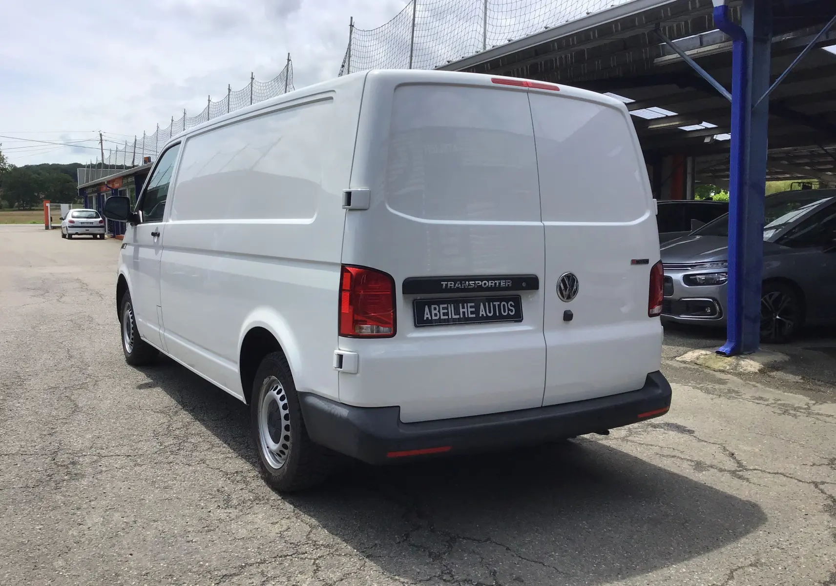 Vue 3/4 arrière droite d'un Volkswagen Transporter 6.1 blanc, fourgon utilitaire avec porte arrière pleine et pare-chocs noir.