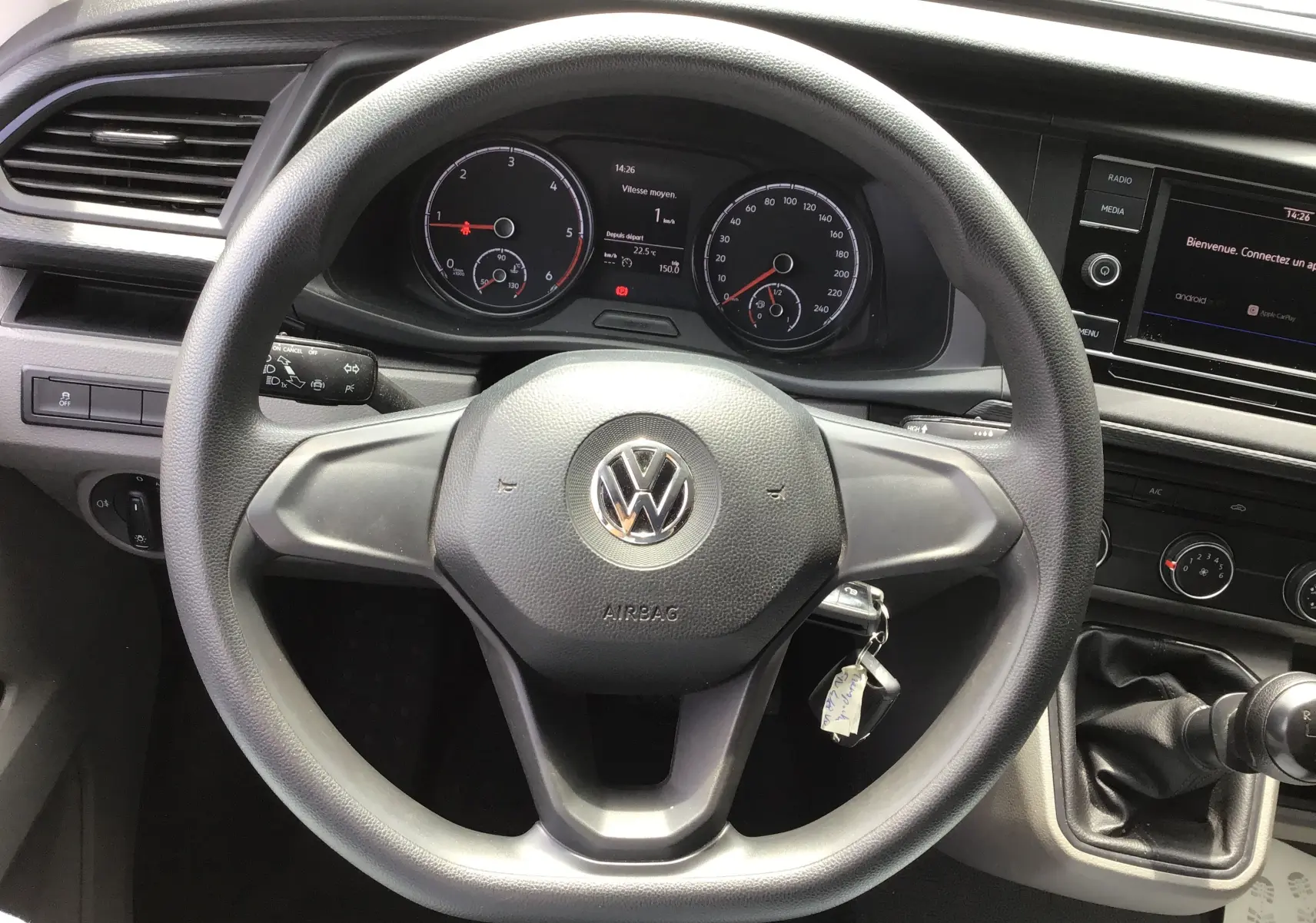 Vue rapprochée du volant noir et du tableau de bord du Volkswagen Transporter 6.1 blanc avec boîte manuelle et écran multimédia.