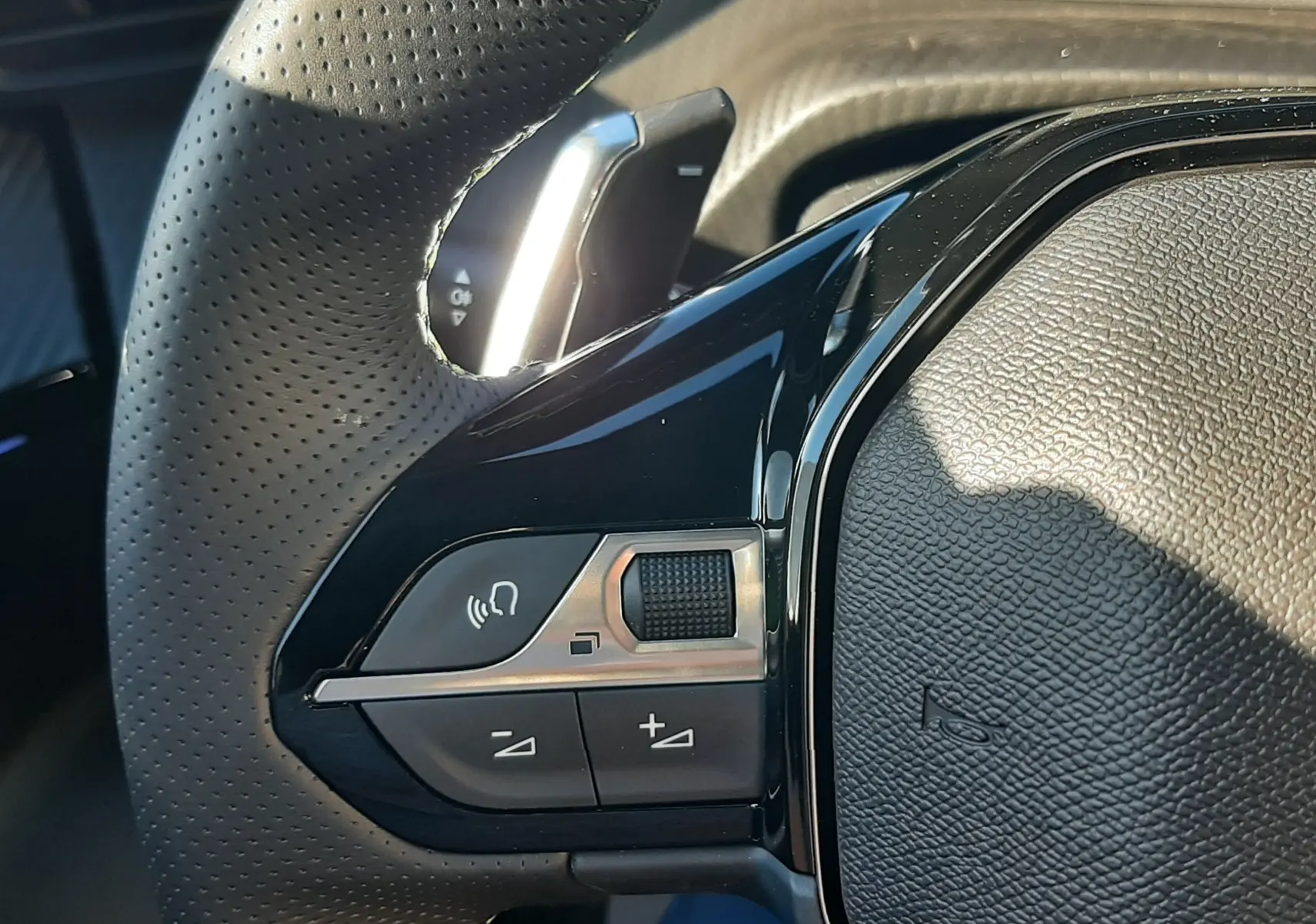 Gros plan sur la partie gauche du volant perforé noir du Peugeot 2008 gris Selenium, avec commandes intégrées et palettes de changement de vitesse.