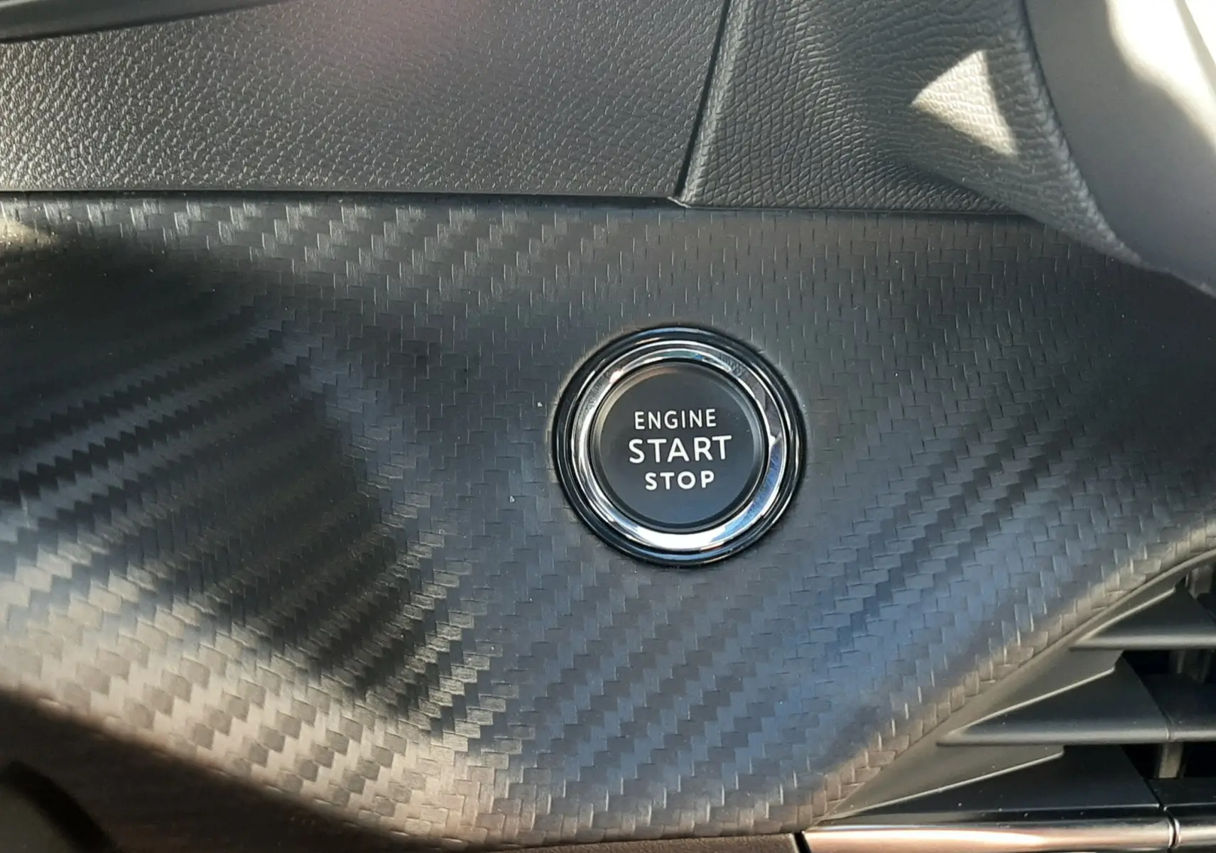 Bouton démarrage moteur circulaire sur tableau de bord effet carbone noir du Peugeot 2008 hybride 2025.