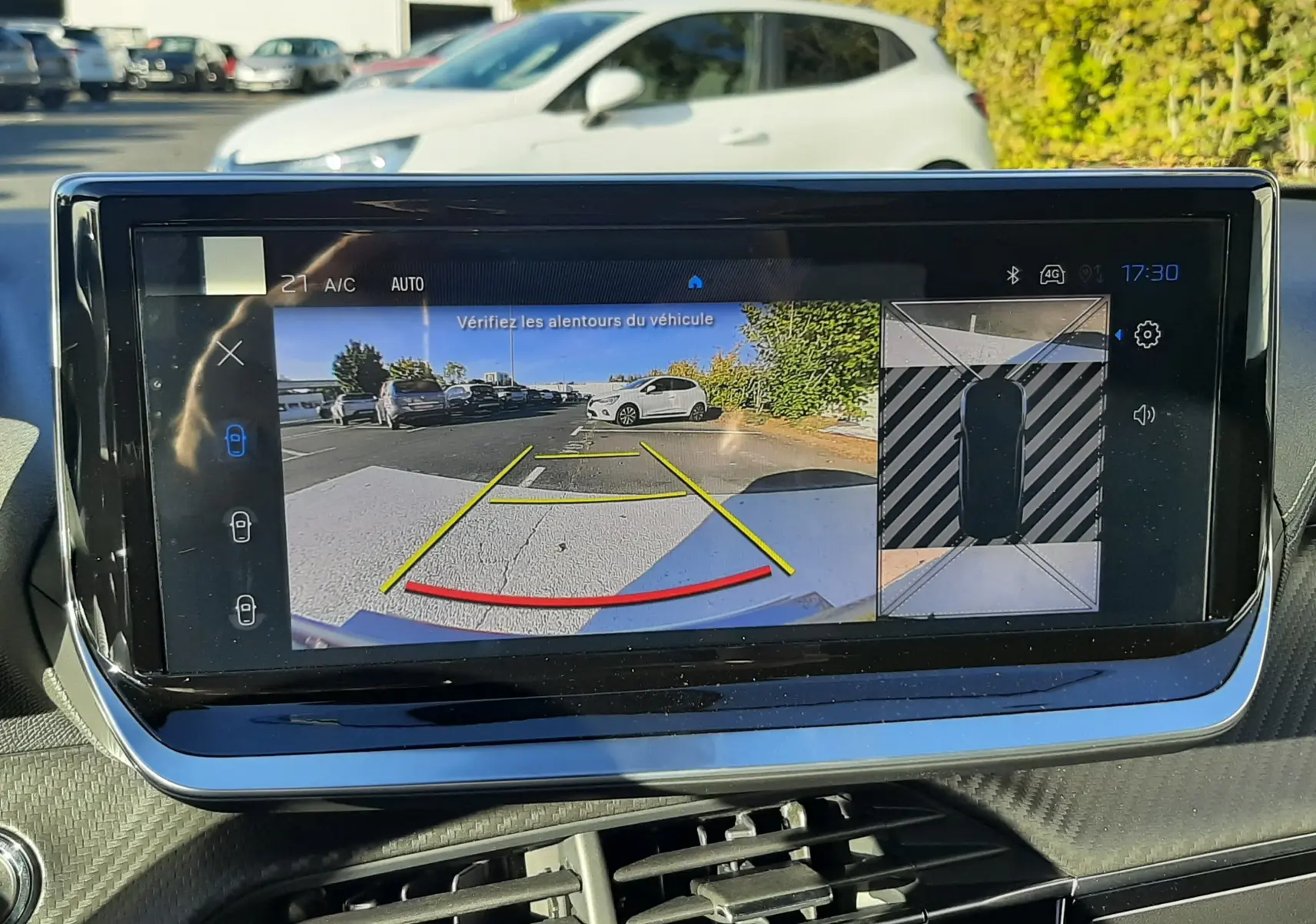 Écran intérieur affichant la caméra de recul avec vue 3/4 arrière droite d'un Peugeot 2008 gris selenium en extérieur.