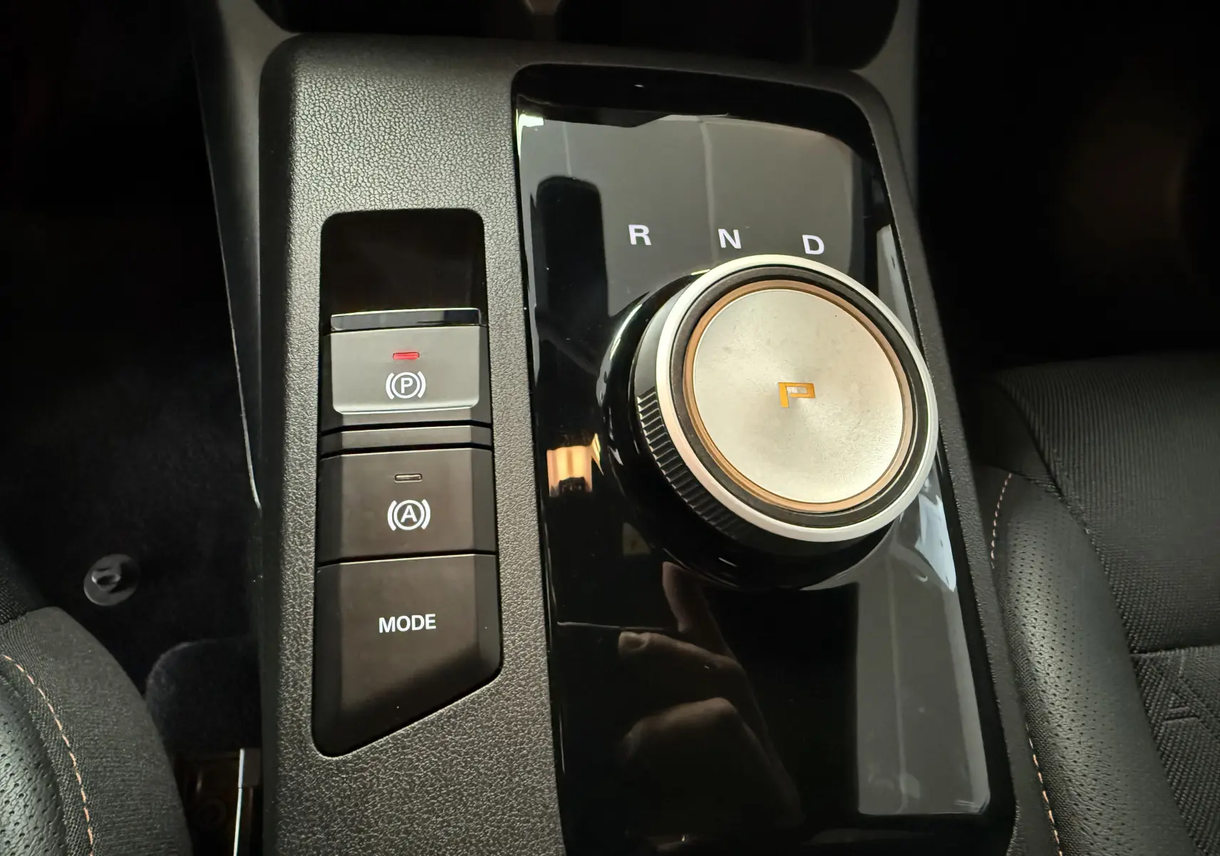 Gros plan sur la molette de boîte automatique et les boutons de contrôle du frein à main dans l’habitacle noir du MG3 Hybrid+ Luxury.