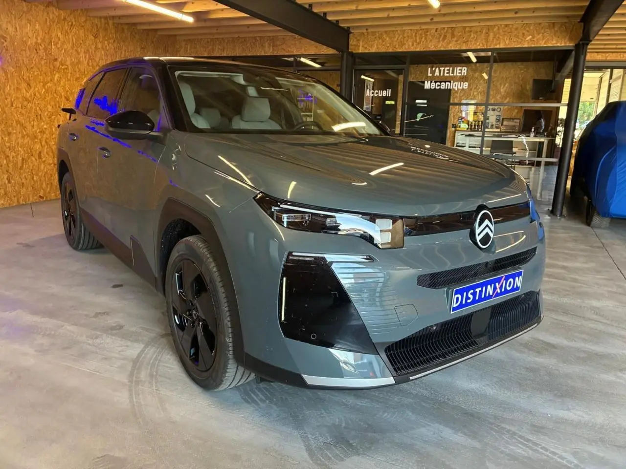 Vue 3/4 avant d'un Citroën C5 Aircross 2026 vert avec détails noirs et jantes noires, stationné en intérieur.