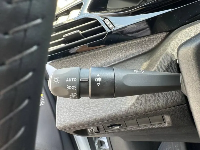 Gros plan sur la commande des phares et clignotants côté gauche du tableau de bord intérieur gris du Peugeot 308 bleu.