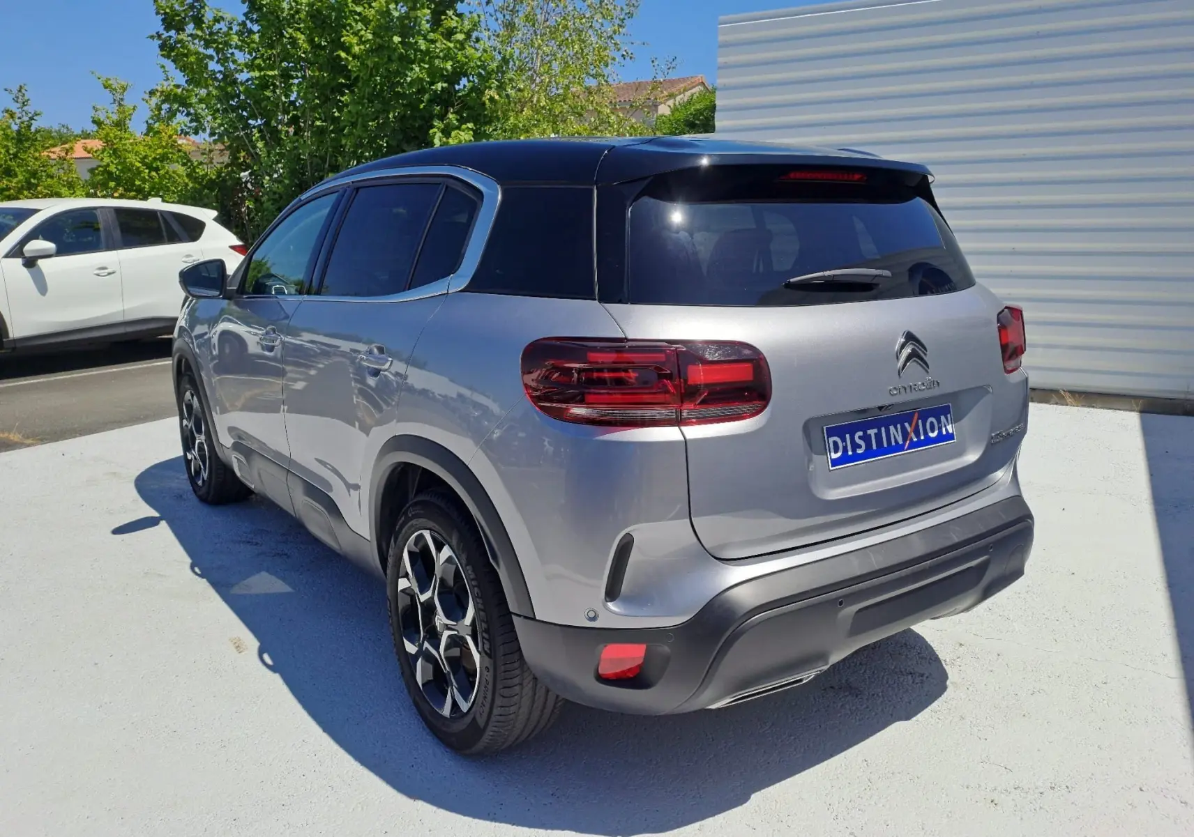 Vue 3/4 arrière droite d'un Citroën C5 Aircross gris Artense avec toit noir et jantes bi-ton sur parking.