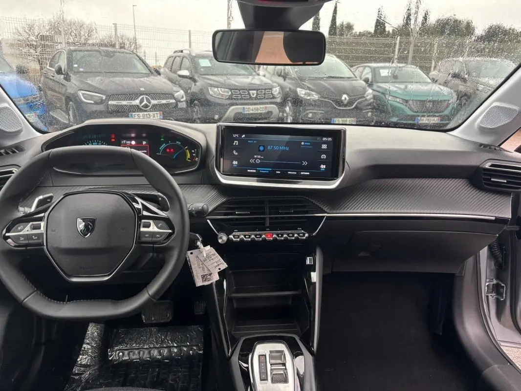 Vue intérieure frontale du poste de conduite gris de la Peugeot 208 Hybrid 100 e-DCS6 Style avec écran tactile et volant multifonction.